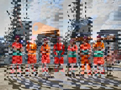 Seven Tideway employees wearing PPE, standing on a building site with a very large, tall piece of construction machinery behind them