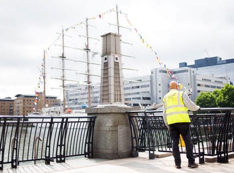 An RSE Building Services employee standing in front of black railings, looking at a large sailing ship in one of the London docks