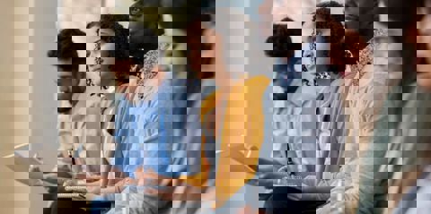 A diverse group of five employees sitting in a row, listening to a Mates in Mind presentation on mental health, and making notes