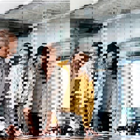 Three employees standing in an office with a glass wall, discussing a Mates in Mind report which is open on the desk in front of them